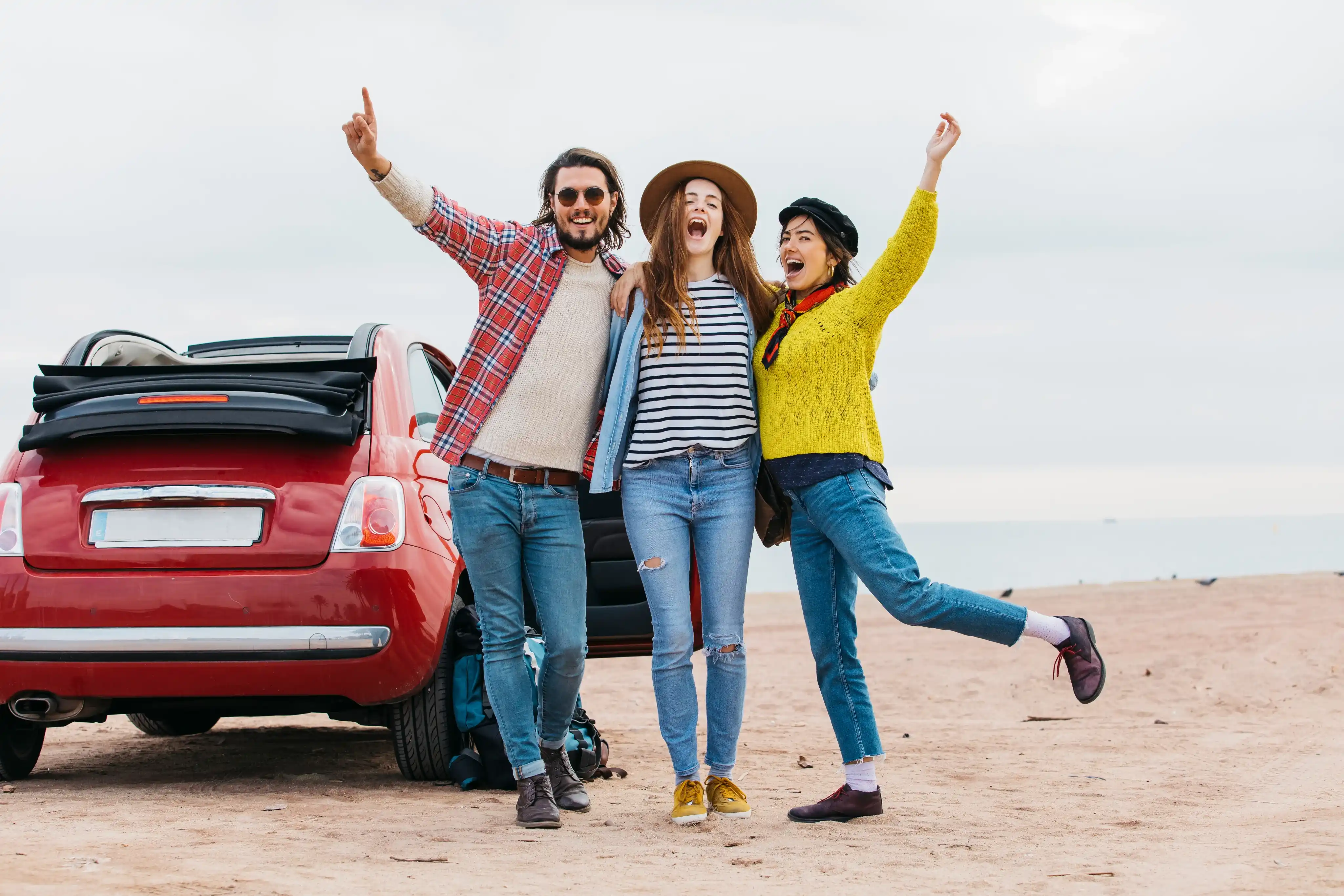 Group of happy friends with red car on beach